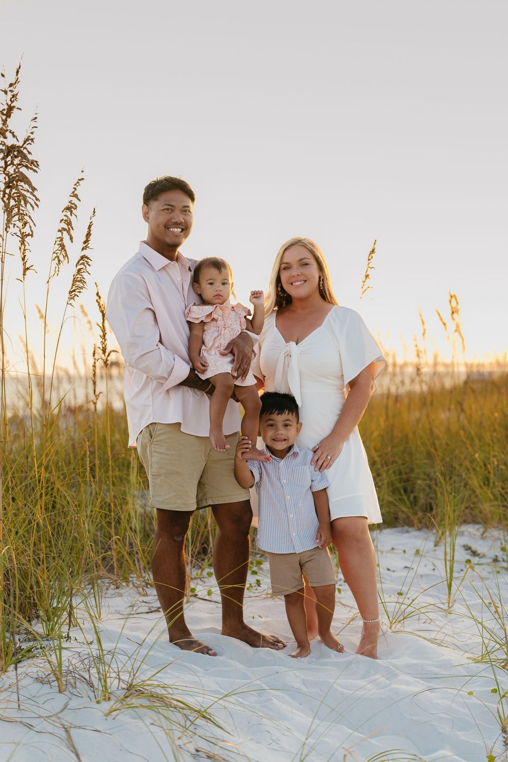Family enjoying sunset together on white sand beach with sea oats swaying in golden light.