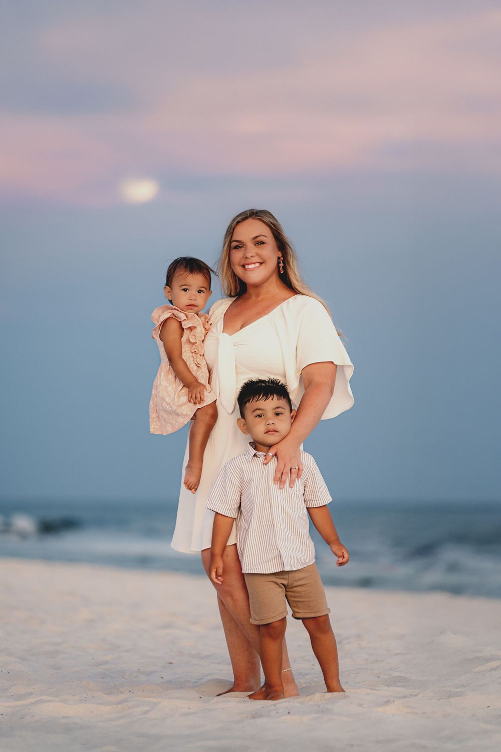 Family enjoying sunset together on white sandy beach with ocean in background during golden hour.