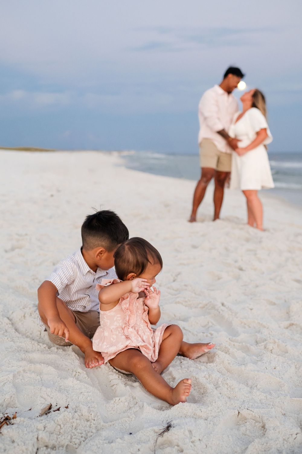 A couple shares romantic moments together on a white sandy beach during a sunset photoshoot.