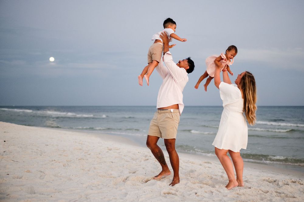 Family in white outfits playing and dancing together on a sunny beach during sunset photoshoot.