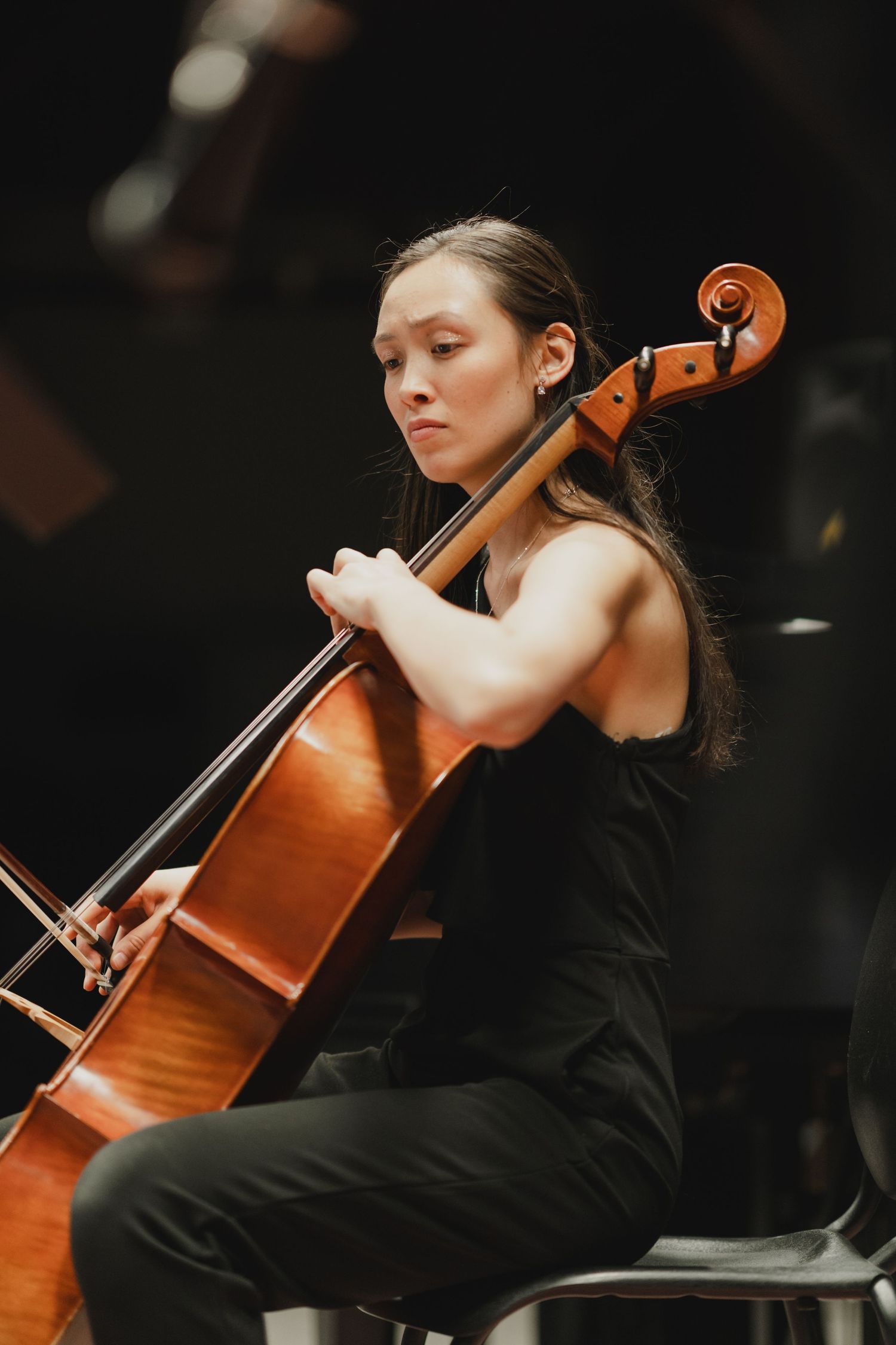 Cellist in black dress performs with wooden instrument during classical concert.