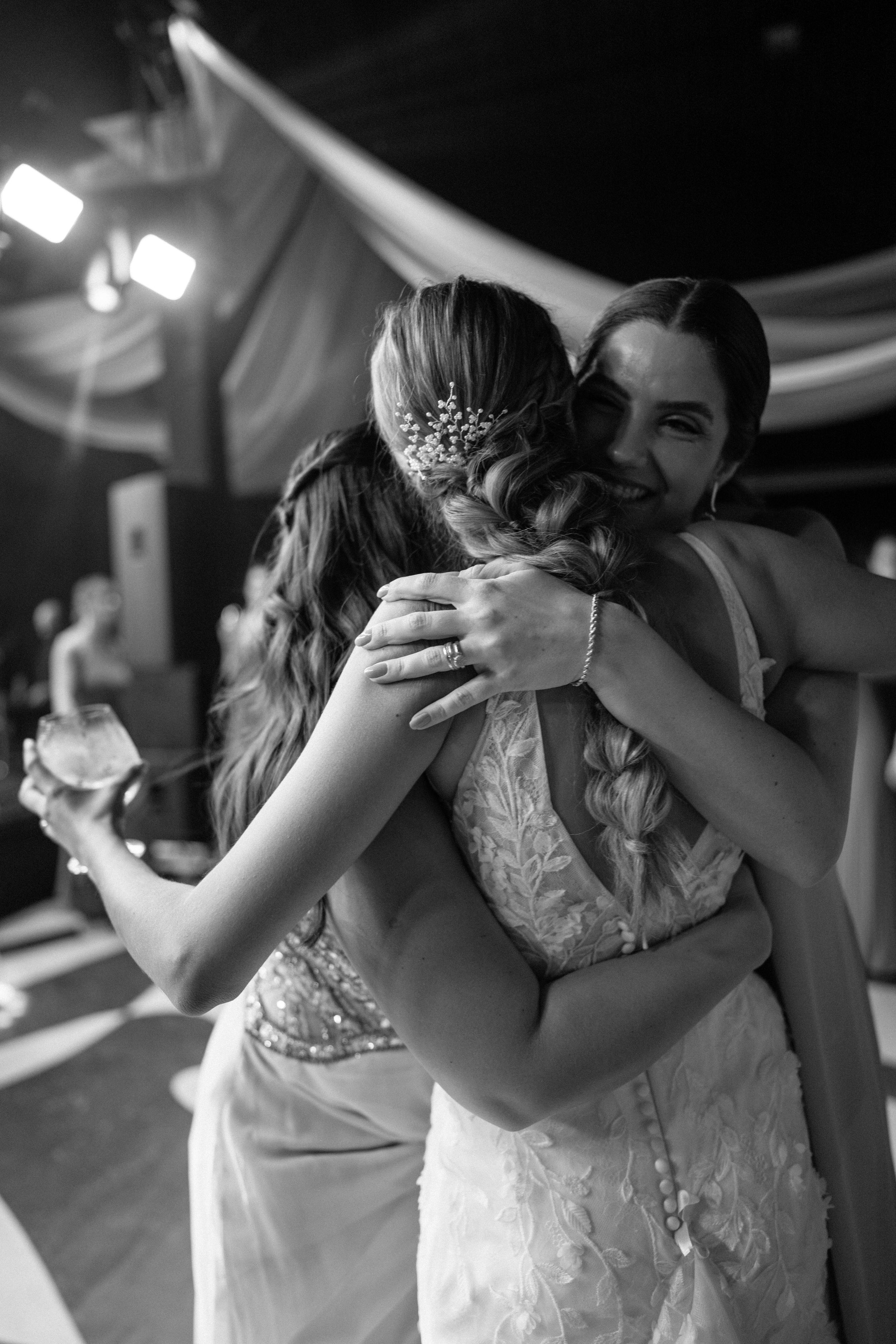 Two people share an emotional embrace at a wedding reception under draped fabric decor in black and white photography.