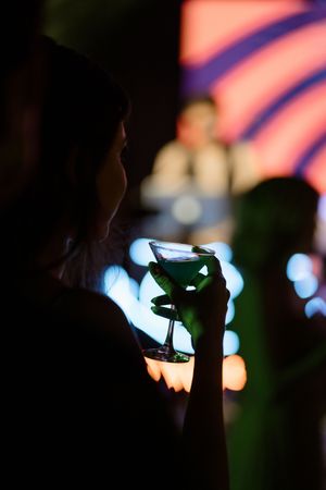 Silhouette of person holding a martini glass with blue bokeh lights and stage backdrop in background.