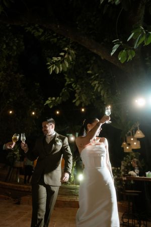 A couple shares a romantic dance under twinkling lights at an outdoor evening wedding reception.