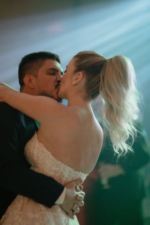 A romantic wedding couple shares a passionate kiss on the dance floor under atmospheric blue lighting.