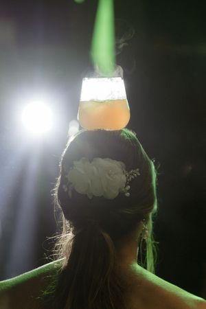 A glass of beer balanced on someone's head with dramatic backlighting and green accent lighting creating a silhouette effect.