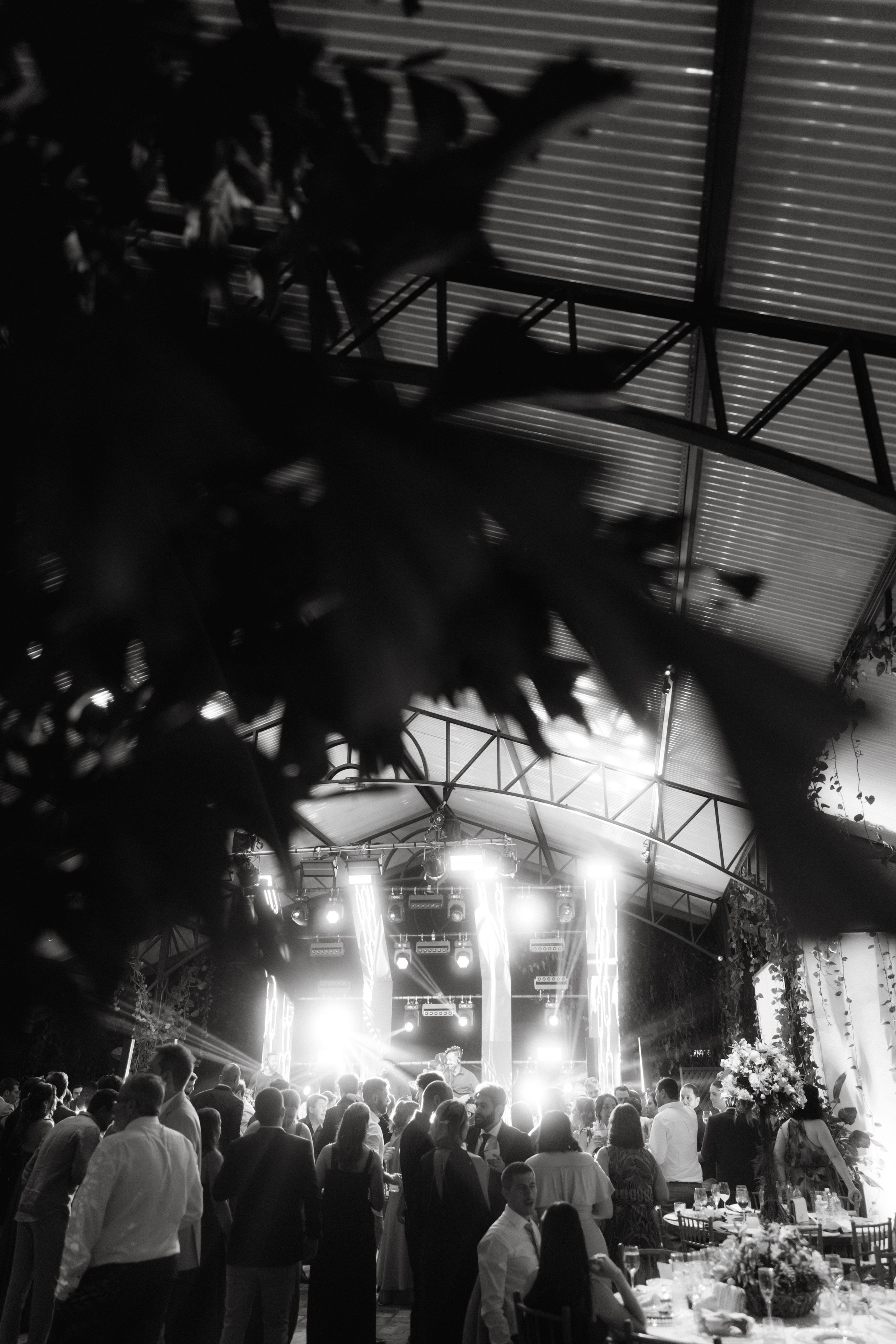 A dimly lit wedding reception venue with bright stage lights illuminating a crowded dance floor during an evening celebration.