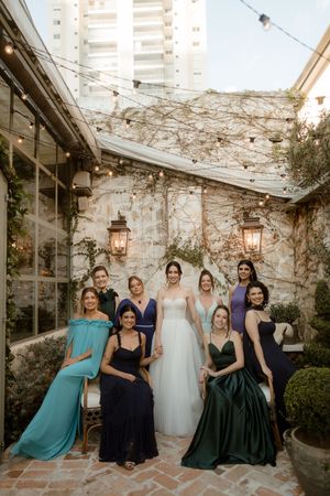 A bridal party poses in a rustic courtyard with stone walls, lanterns and climbing vines at sunset.