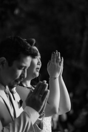 A black and white photograph captures two people in prayer with their hands clasped together.