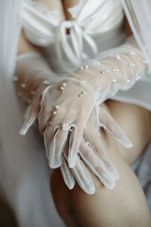 Close-up detail of delicate white bridal gloves adorned with small pearl embellishments.
