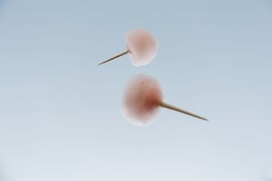 Pink cotton candy on sticks against a soft blue background creates a dreamy, minimalist composition.
