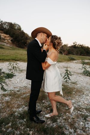 A romantic couple shares a kiss in a field of white wildflowers at sunset.