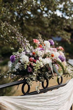 Elegant floral centerpiece with purple, pink and white flowers arranged in black letters on flowing white fabric.