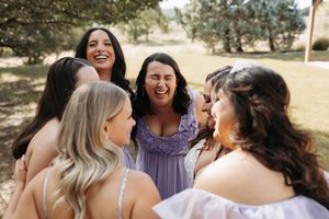 A group of wedding guests share a candid laughing moment together outdoors in natural lighting.