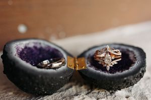 Two engagement rings displayed inside a split purple geode crystal against a textured gray surface.