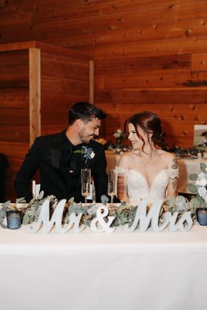 A romantic moment shared at a rustic wooden wedding reception venue with 'Mr & Mrs' decor visible on the table.