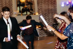 Guests dancing with glowing lightsabers create colorful light trails in a dimly lit brick-walled venue.
