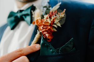 A delicate orange and green boutonniere being pinned to a dark suit jacket lapel.
