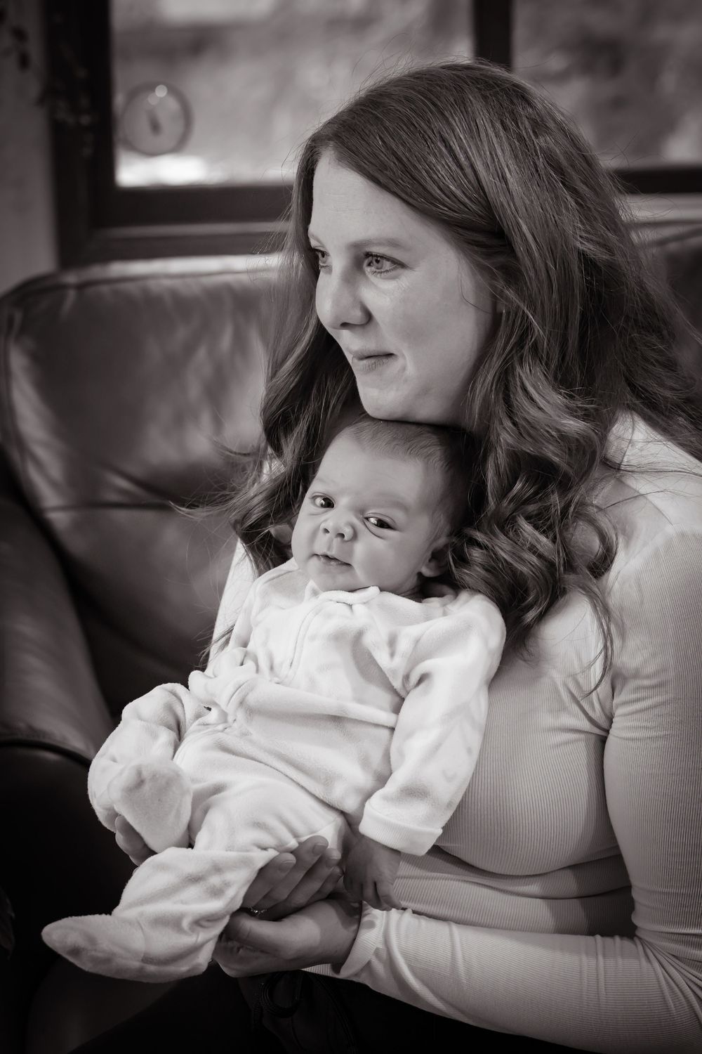 Baby in white clothing resting peacefully on a leather couch during an intimate photo session.