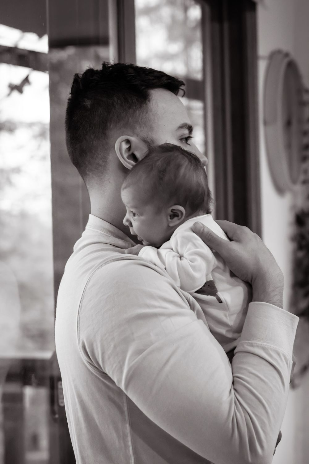 Close-up black and white portrait of a person holding and kissing a baby in a white outfit.