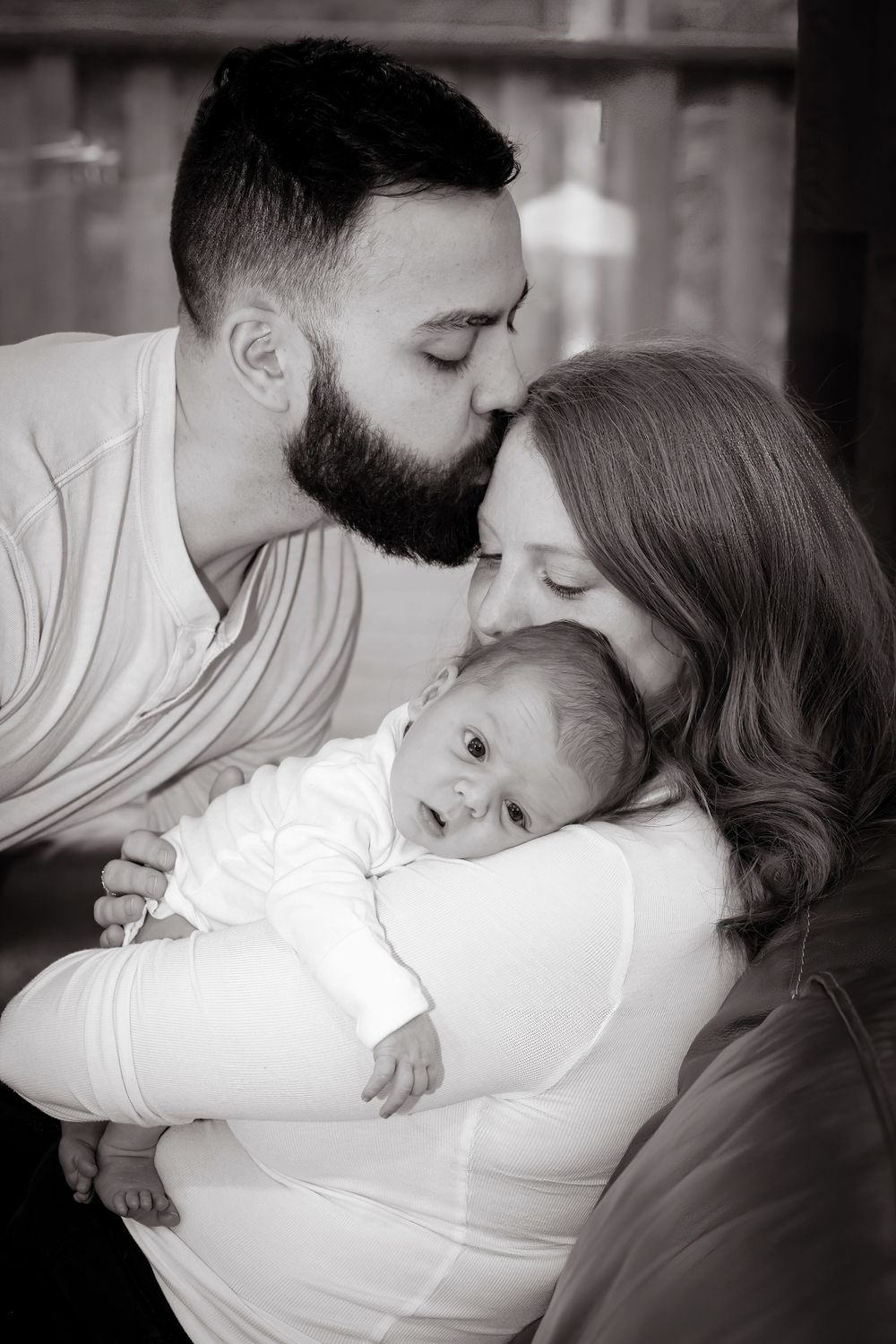 Tender black and white moment of parents sharing affection with their newborn baby.