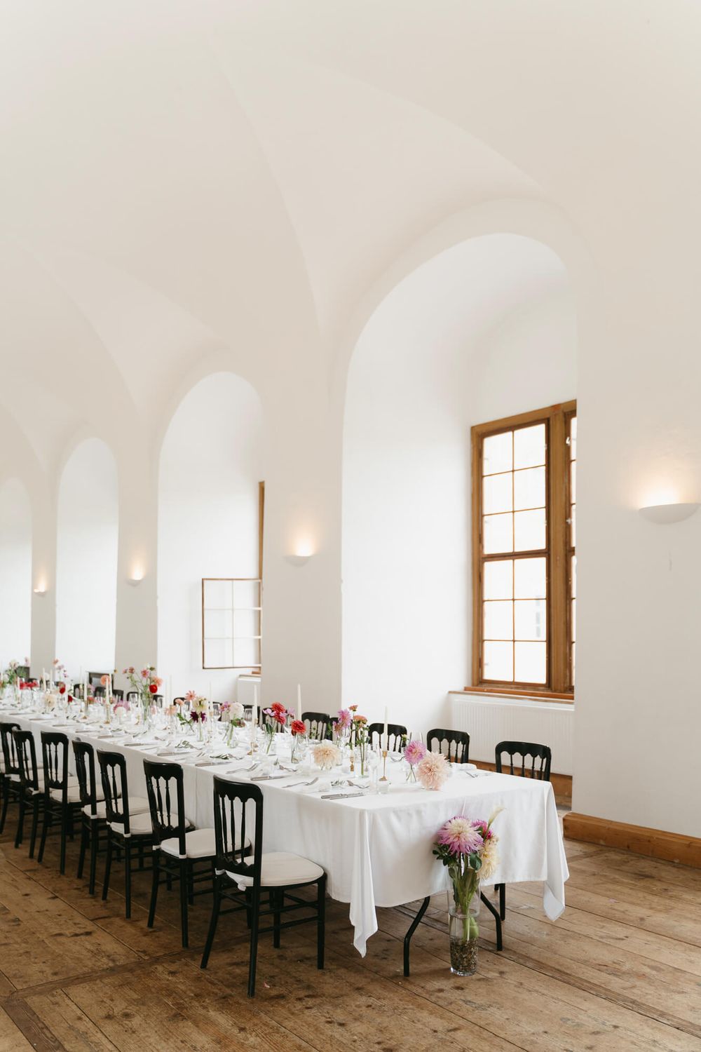 White arched dining room with rustic wooden floors and black chairs set for an elegant wedding reception.