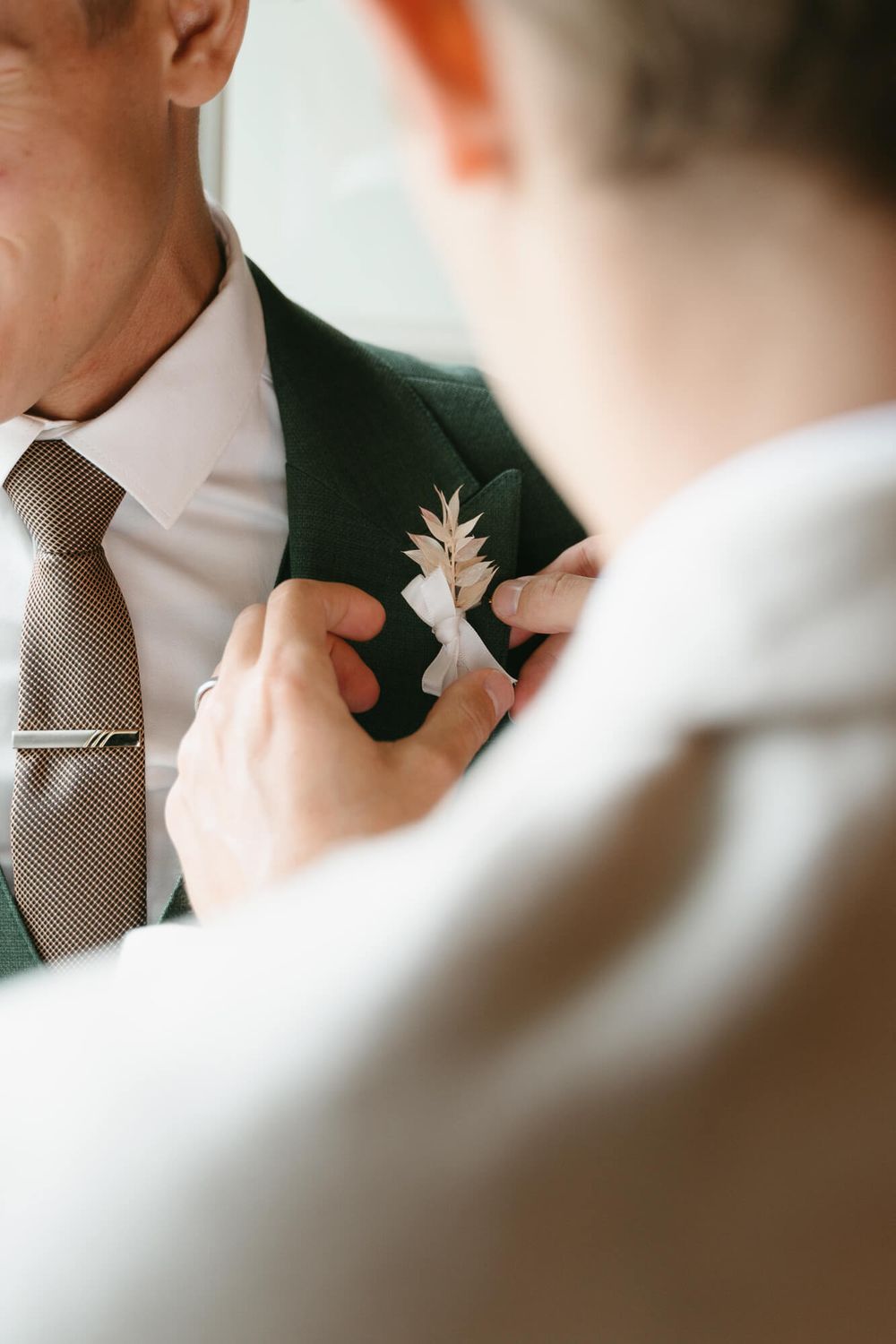 Close-up shot of someone adjusting a brown tie and boutonniere on a formal suit jacket.