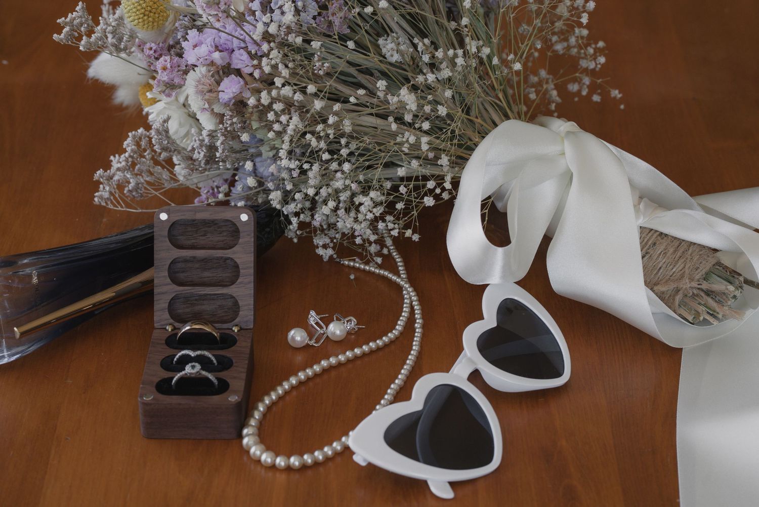 Wedding accessories including pearl necklace, ring box, baby's breath flowers and heart decorations on wooden surface.