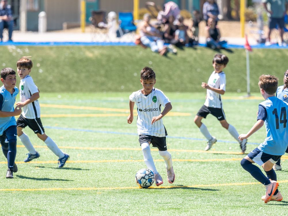 Children playing soccer on a sunny grass field during a youth sports event.