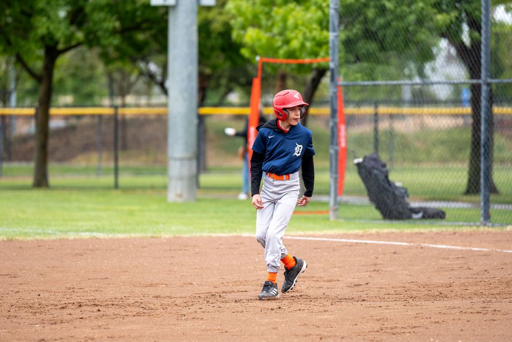 Young baseball player in blue uniform runs bases on dirt infield during game.