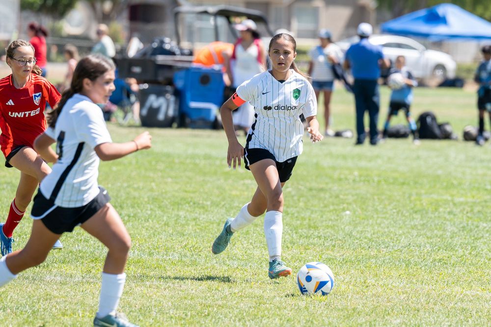 Youth soccer players chasing after a ball during a match on grass.