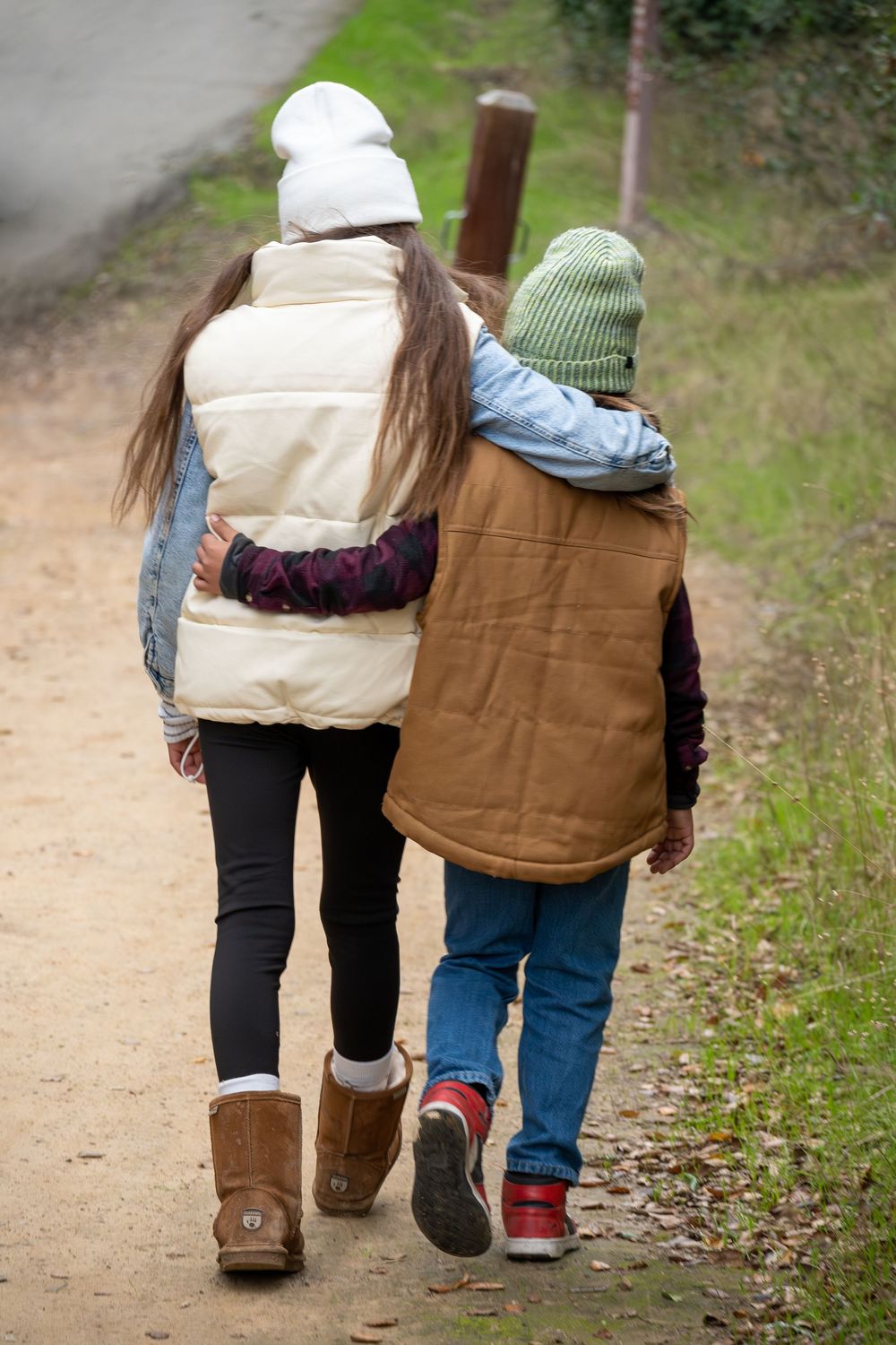 Back view of two people walking together on a path wearing winter boots and vests.