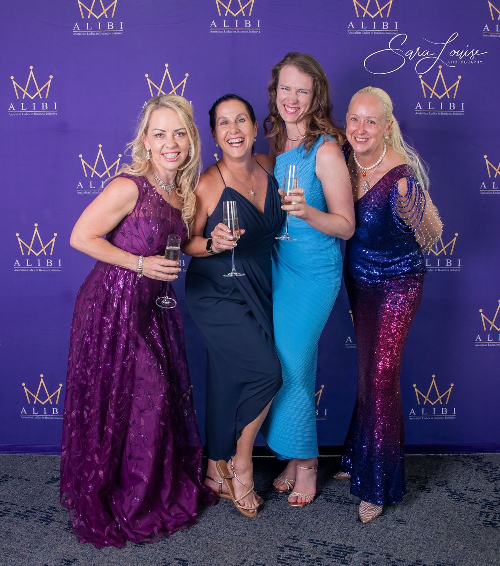 Friends in formal dresses posing together against purple backdrop with crown logos.