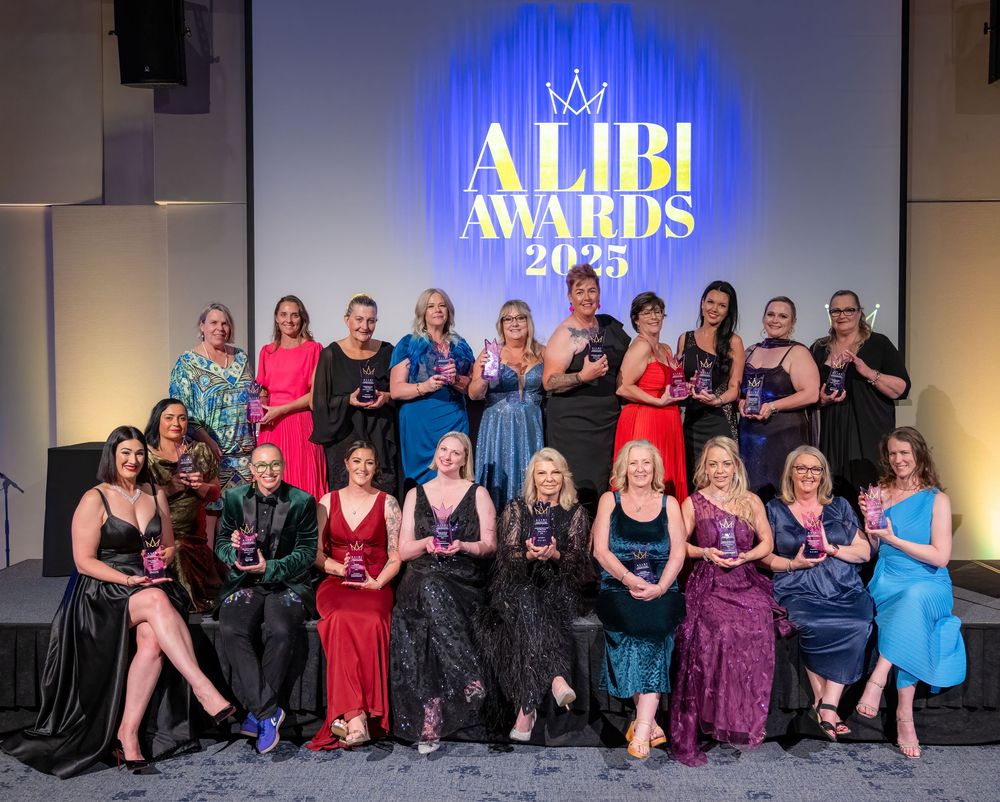 Large group photo at awards ceremony with attendees in formal attire against blue backdrop.