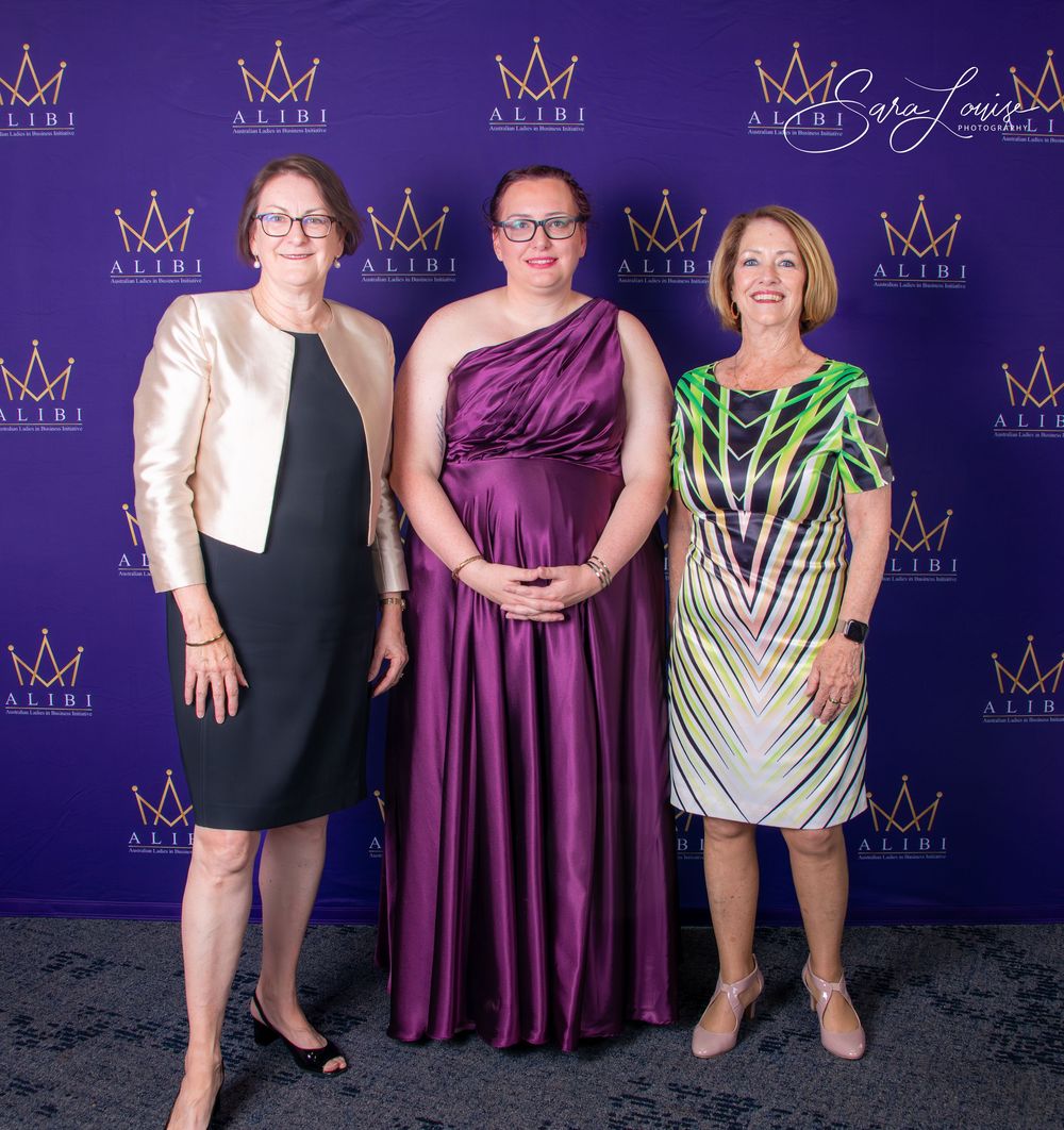 Group photo of attendees in elegant evening wear against purple backdrop with crown logos.