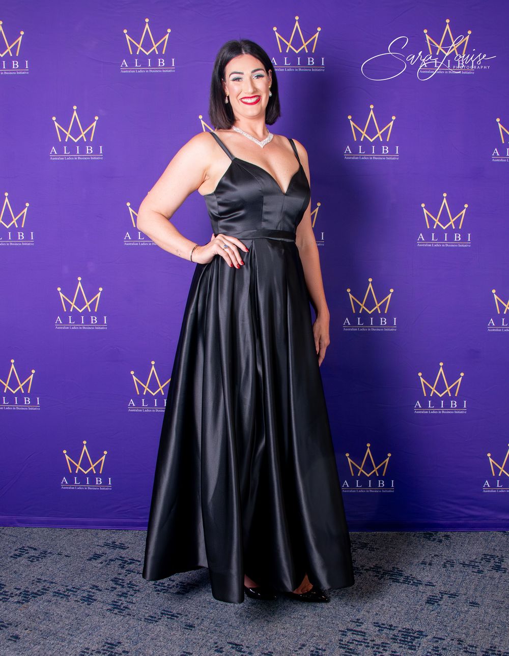 Women in formal black dresses posing against purple backdrop with crown logos.