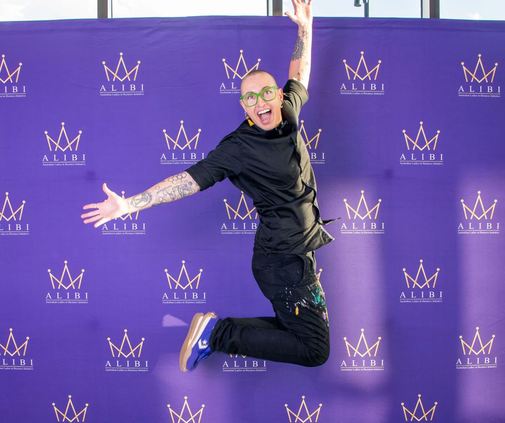 Energetic jumping pose against purple backdrop with crown logos at formal event.