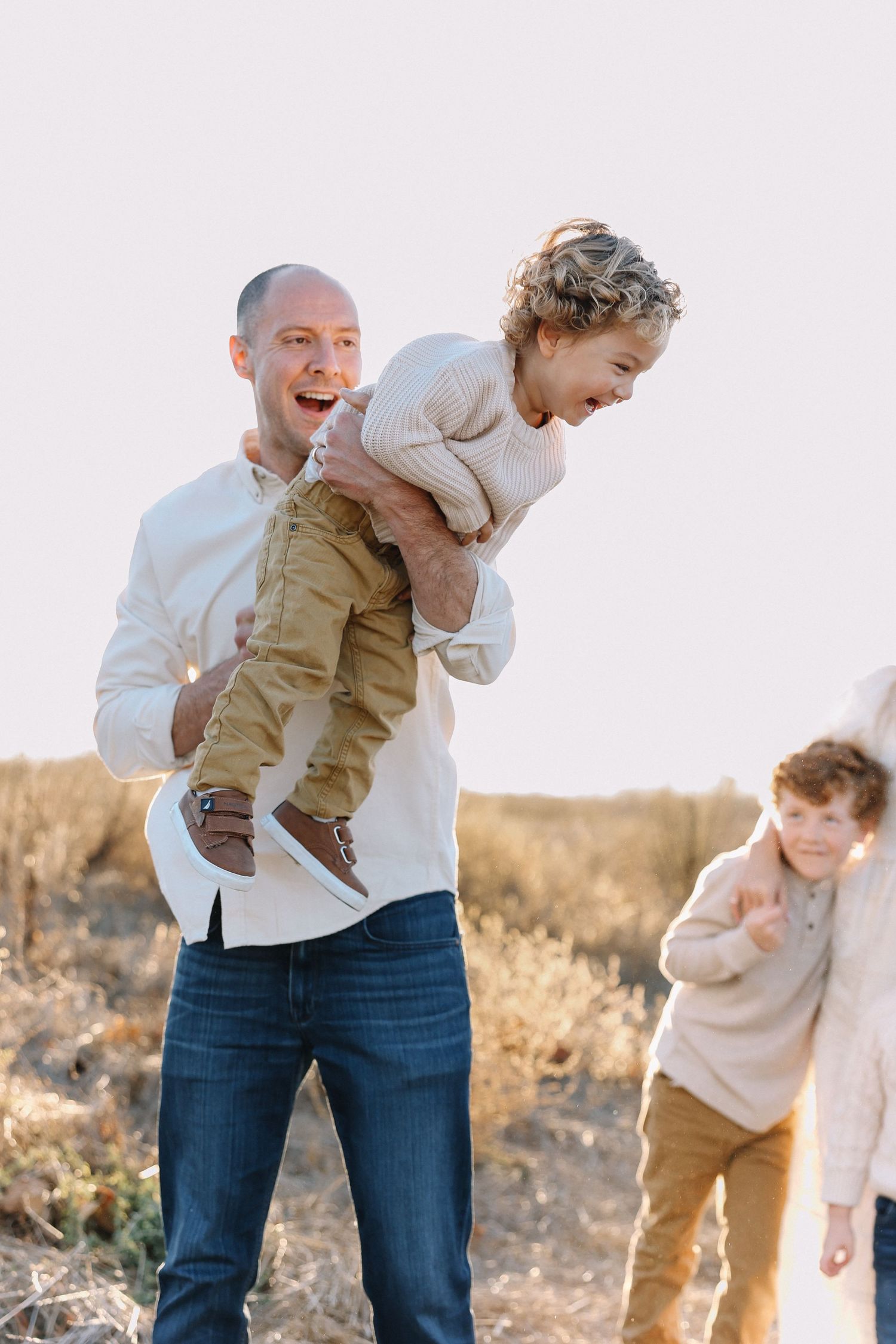 Family playing together in a California field surrounded by soft evening light