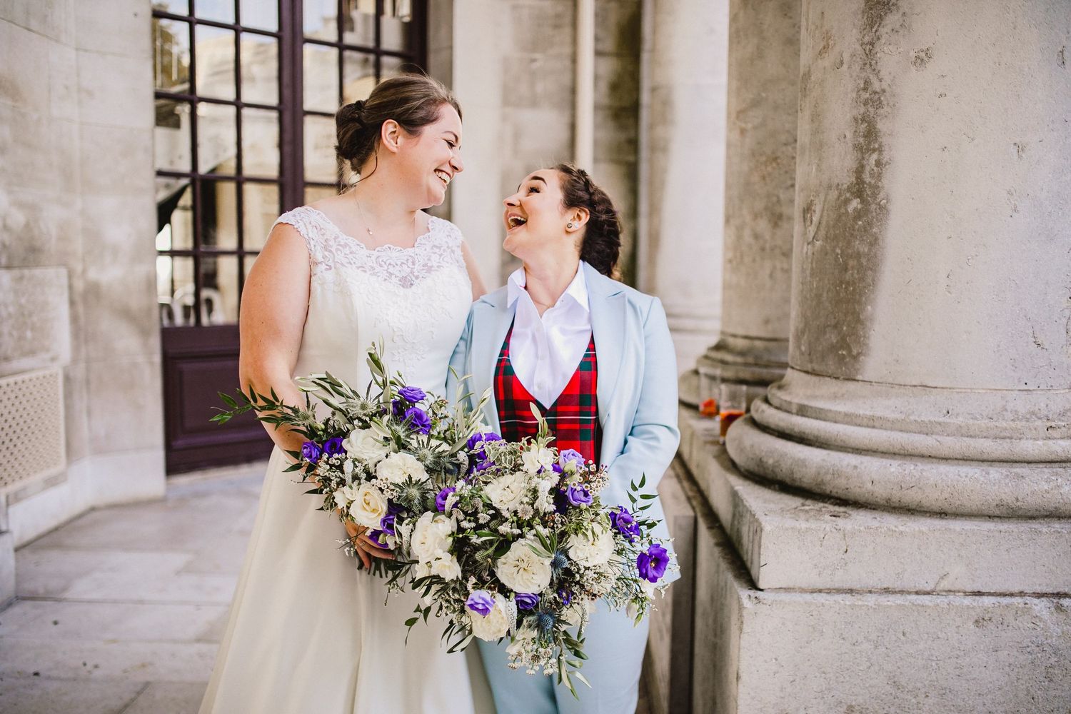 two brides beam happily at each other outside ashton memorial in lancaster's Williamson park after getting married on their wedding day