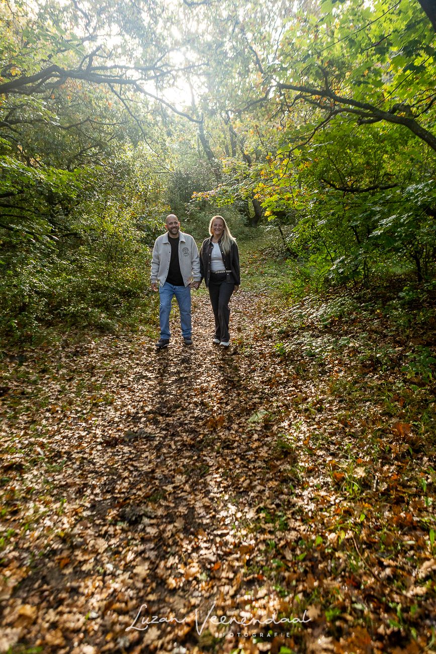 Ouders wandelen hand in hand door het bos bij Johanna’s Hof, met zonlicht door de bomen.