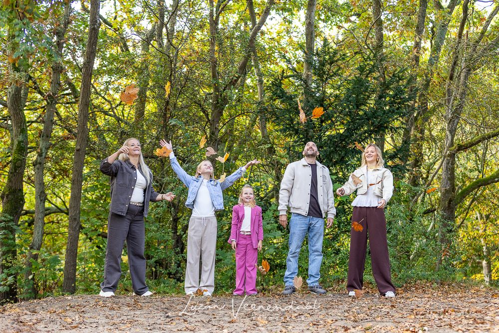 Gezin met drie dochters gooit lachend herfstbladeren in de lucht bij Johanna’s Hof in Castricum