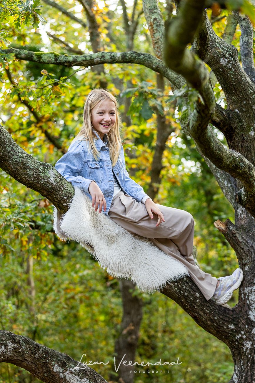 Portret van de middelste dochter (10) zittend in een boom met oranje bladeren om haar heen