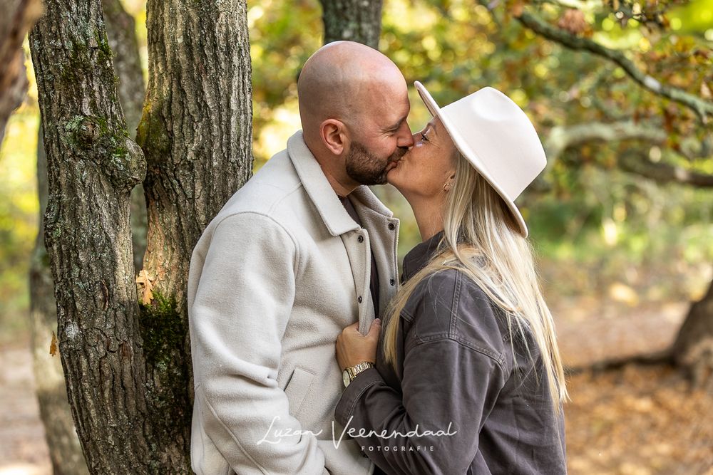 Ouders geven elkaar een liefdevolle kus tussen de herfstkleuren in het bos.
