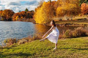 Young woman in white dress dancing by colorful autumn lakeside. Locke Lake Barnstead NH.