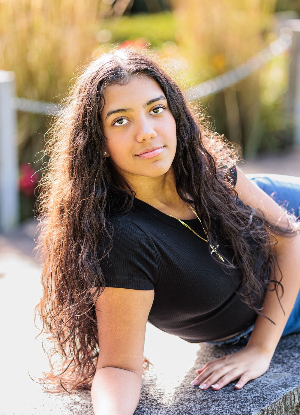 Young woman with long curly dark hair in black top poses outdoors in warm golden sunlight. Cate Park, Wolfeboro NH.
