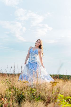 Young woman in blue floral dress standing in golden meadow field. Wells Reserve at Laudolm Wells ME.