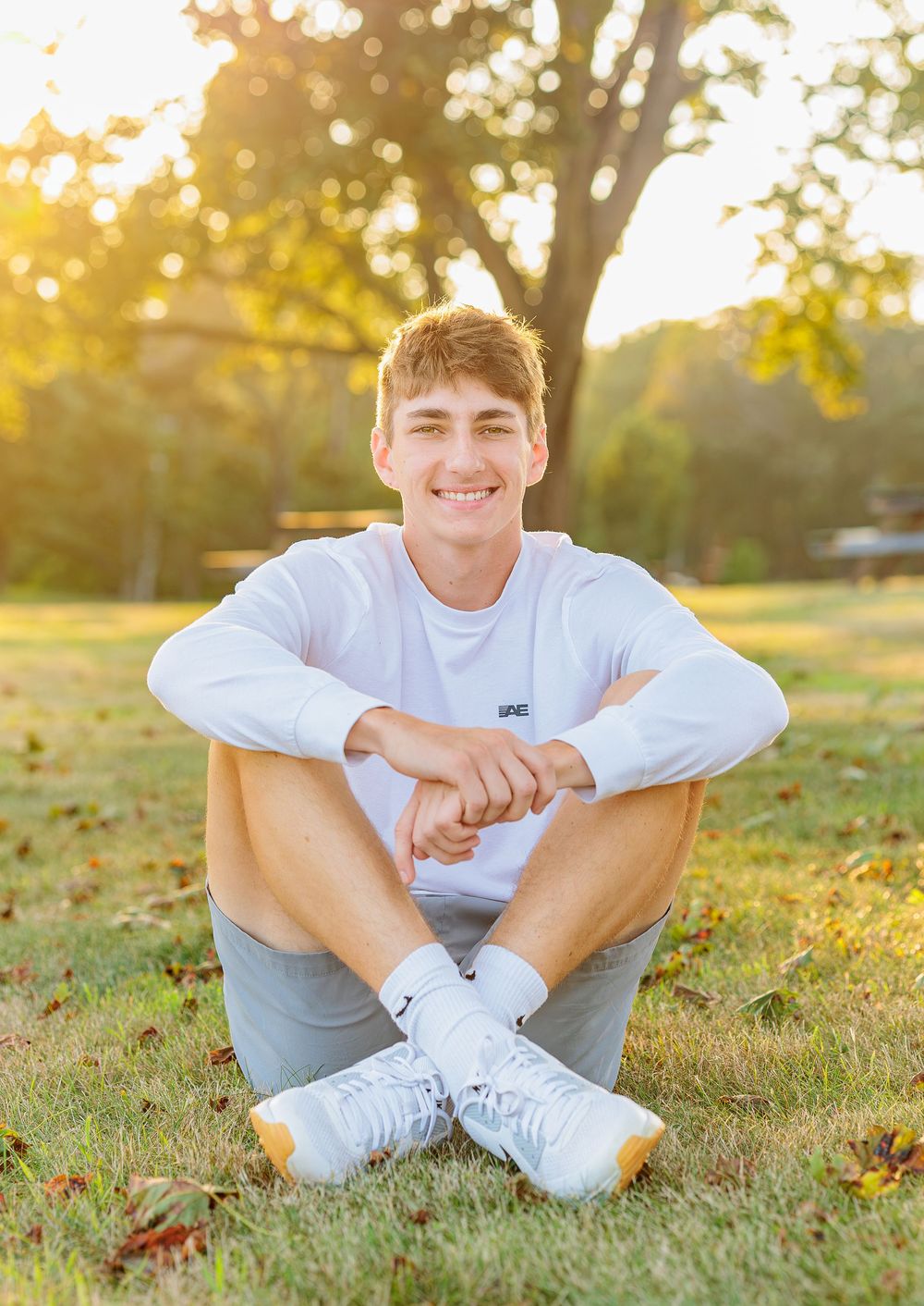 Smiling teen boy in white sweatshirt sitting on grass at sunset. Wells Reserve at Laudolm Wells ME.