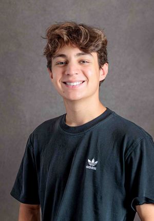 Smiling teen boy in black Adidas t-shirt against gray backdrop.