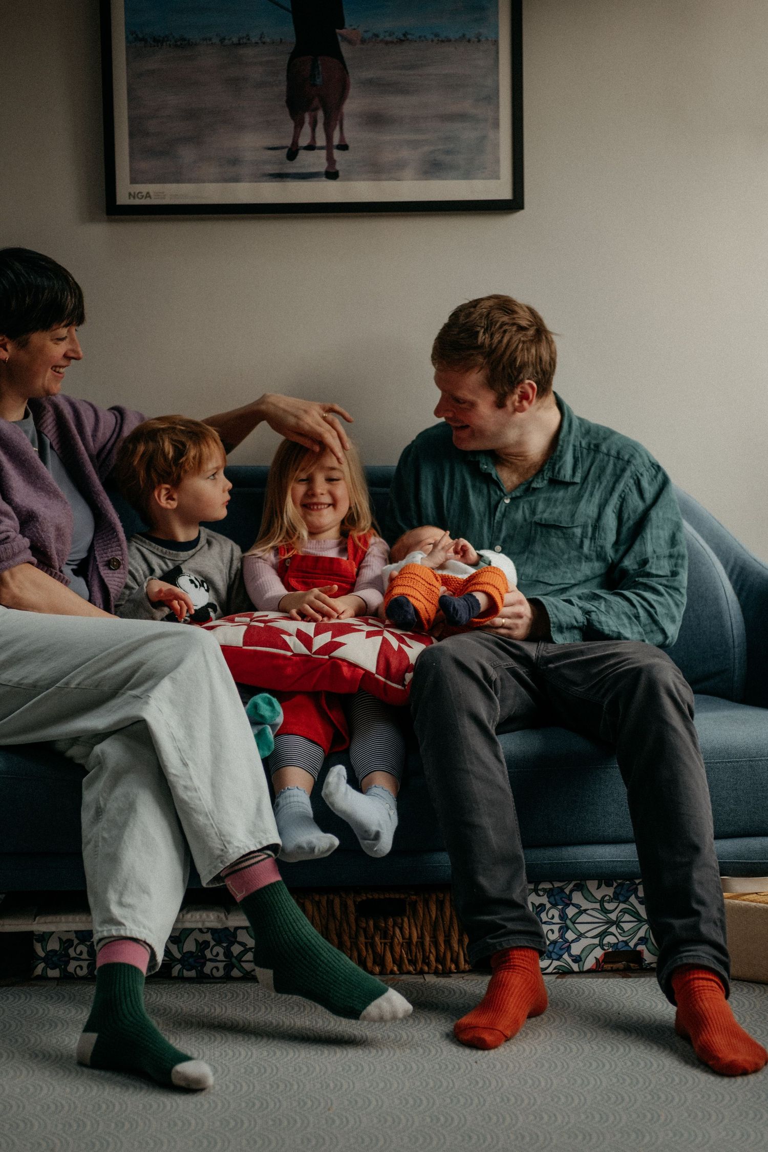 A family of four sitting on the couch, dad holding the brand new little newborn in their home in Gosforth