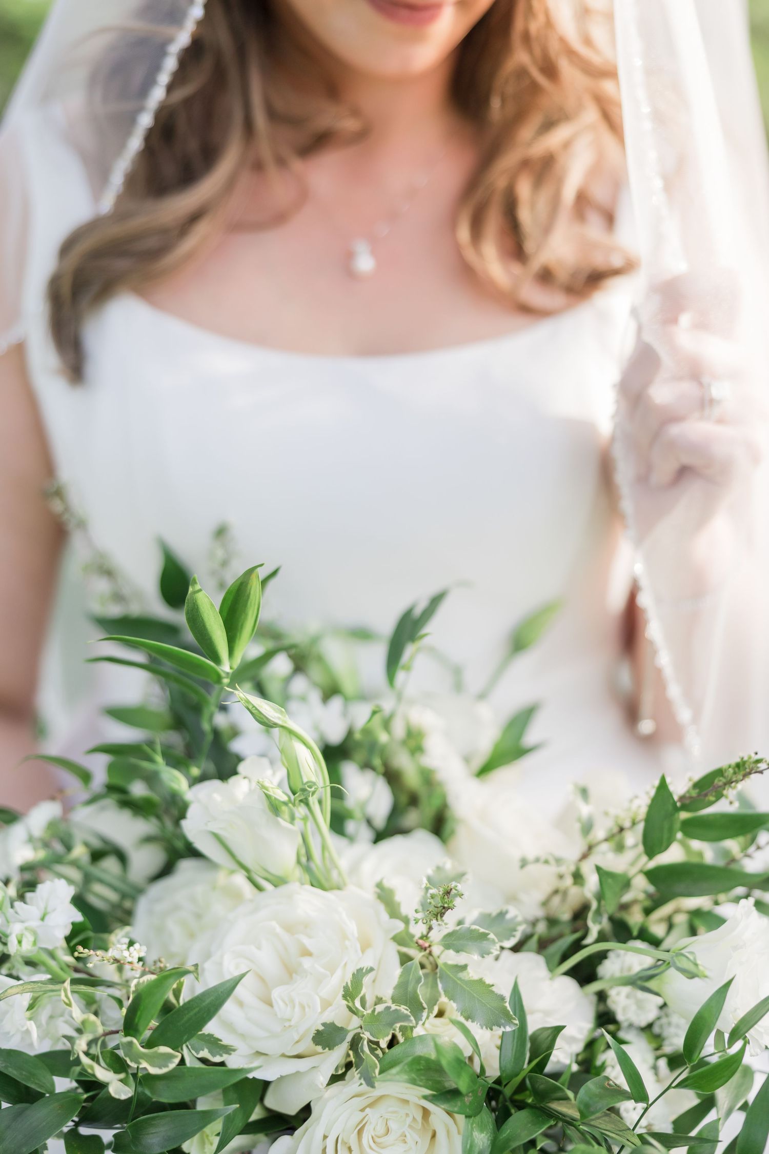 A joyful bride in a white strapless wedding gown holds a beautiful bouquet of peach and pink garden roses with greenery.
